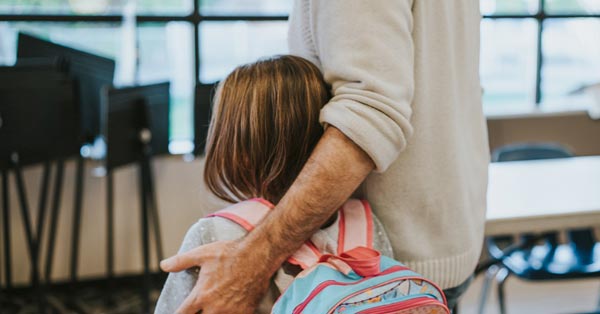 Daughter with a backpack on and father with hand around her